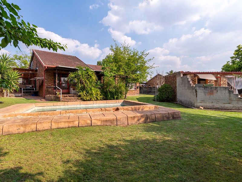 A spacious backyard featuring a swimming pool with stone coping, established lawn, and brick house exterior with a tiled roof.