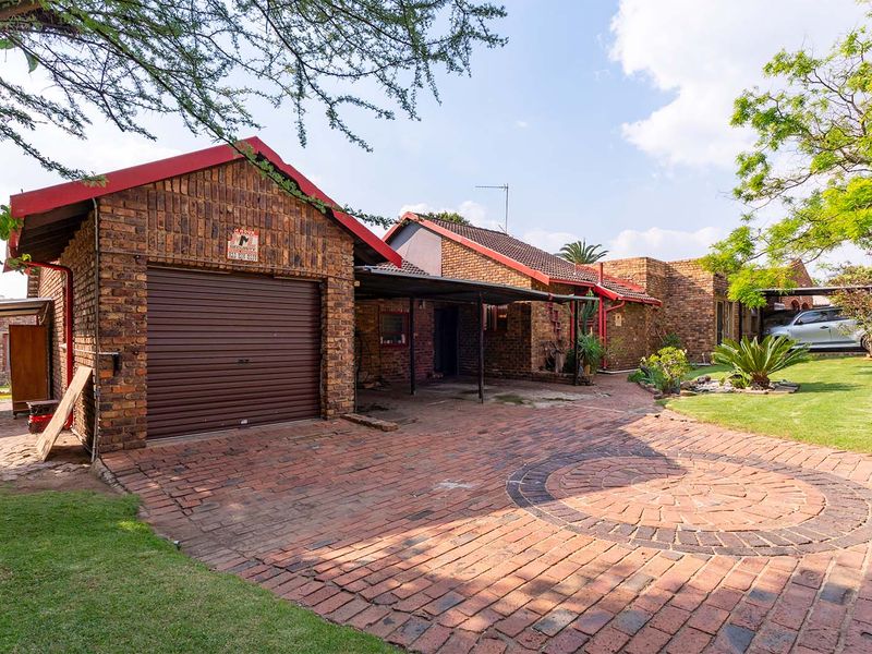 Front view of a face brick house featuring a paved driveway, single garage, and covered carport area set within a landscaped garden.