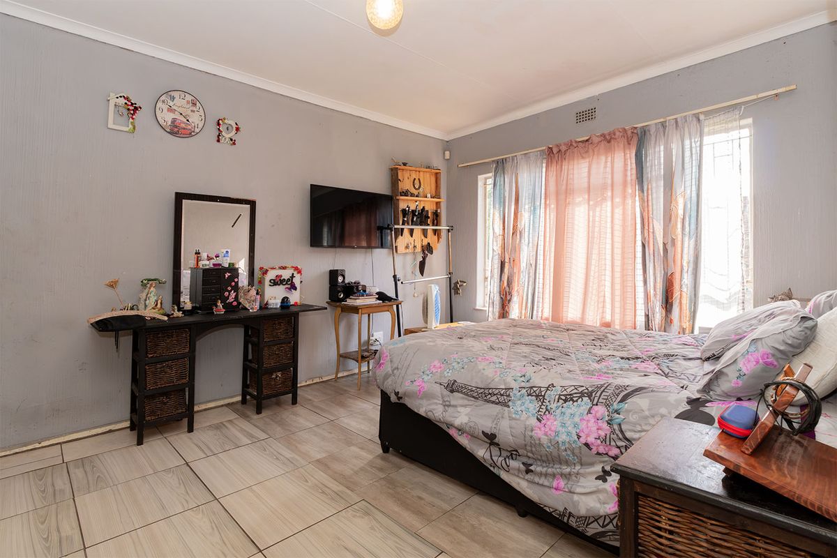 A bedroom featuring tiled flooring and large windows with security bars, offering a functional space ready for cosmetic updates and modernization.