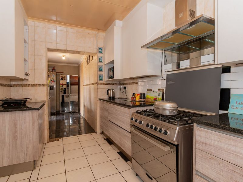 A functional kitchen featuring built-in cabinetry, granite countertops, a gas stove with extractor fan, and tiled finishes throughout.