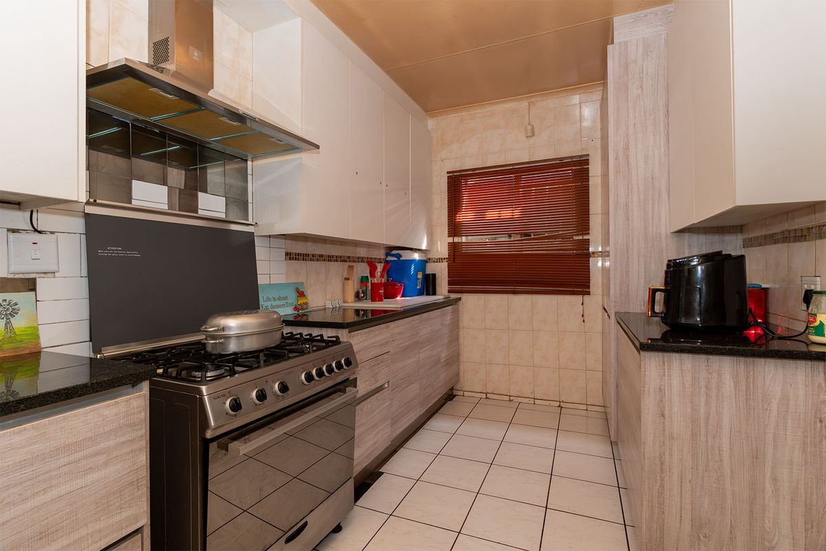 A functional kitchen featuring granite countertops, gas stove with extractor fan, tiled backsplash, and ample built-in cabinetry with a neutral wood-grain finish.
