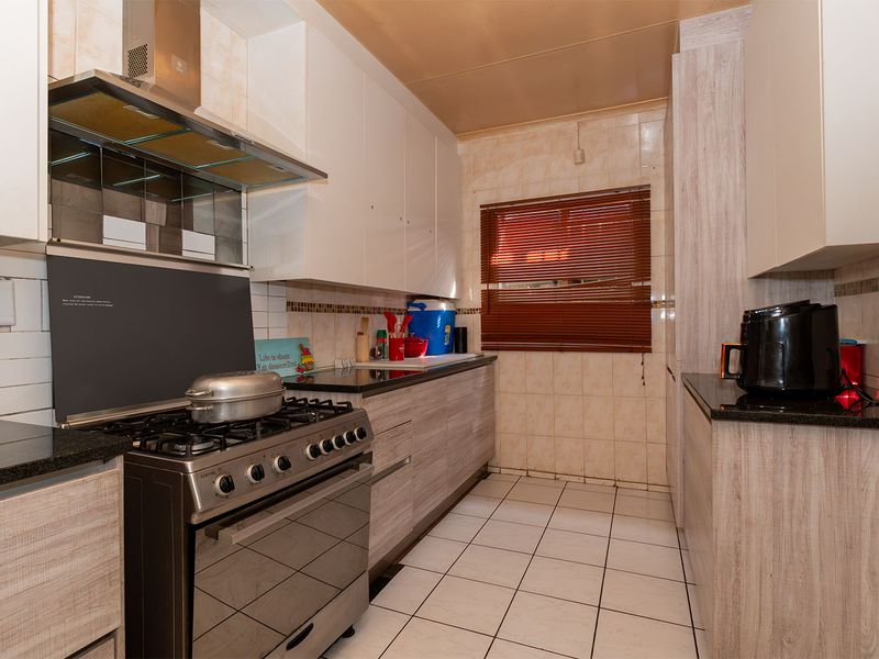 A functional kitchen featuring granite countertops, gas stove with extractor fan, tiled backsplash, and ample built-in cabinetry with a neutral wood-grain finish.