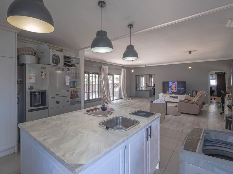 Spacious open-plan living area featuring a central kitchen island with double sink, modern pendant lighting, and seamless flow into the lounge space.
