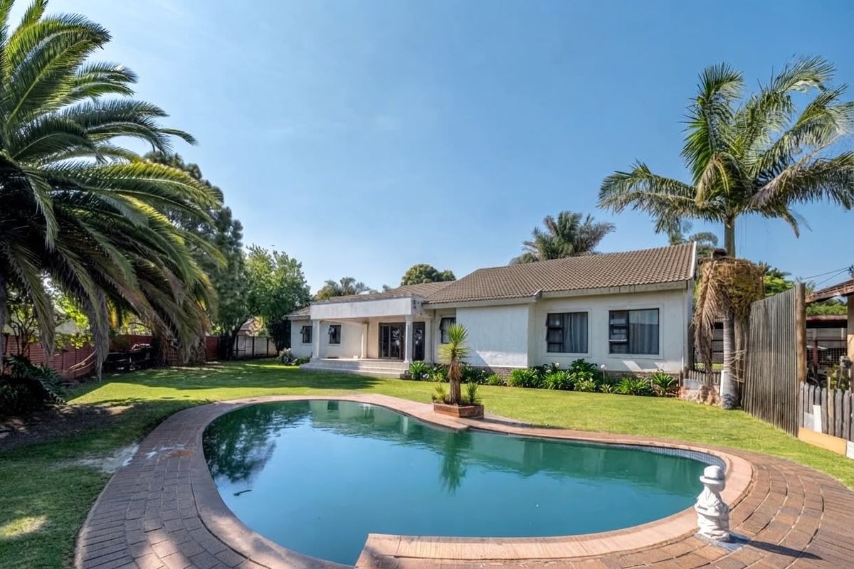Rear view of the property featuring a swimming pool with brick coping, a covered patio area, and a spacious landscaped garden.