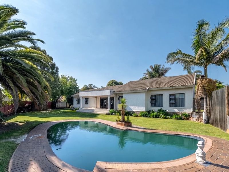 Rear view of the property featuring a swimming pool with brick coping, a covered patio area, and a spacious landscaped garden.