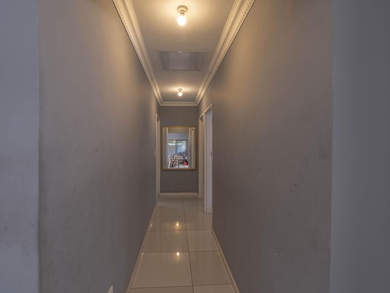 A neutral-toned hallway featuring tiled flooring, crown molding, and recessed ceiling lighting, providing a clean transition between living spaces.