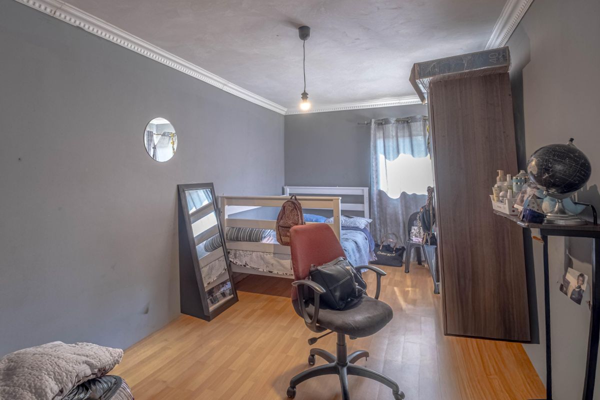 A bedroom featuring laminate flooring, crown molding, and grey painted walls, offering a functional space with potential for cosmetic updates.