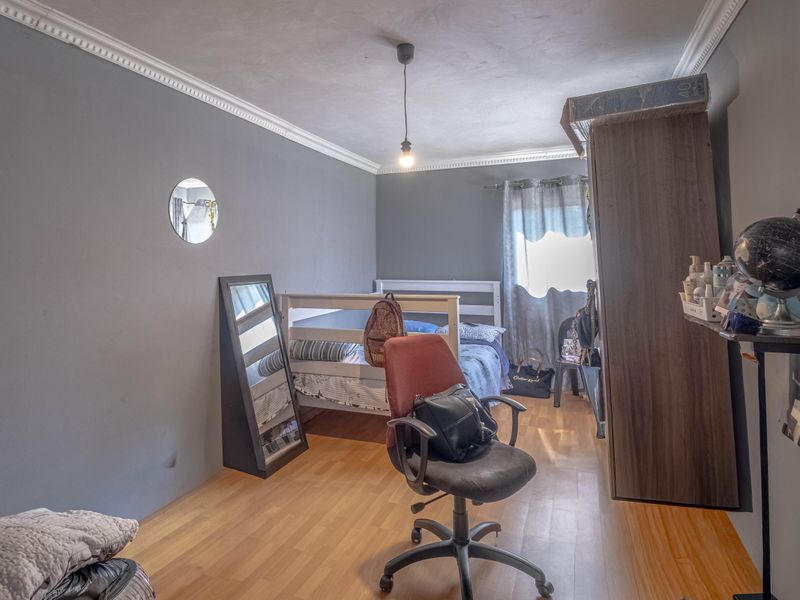 A bedroom featuring laminate flooring, crown molding, and grey painted walls, offering a functional space with potential for cosmetic updates.