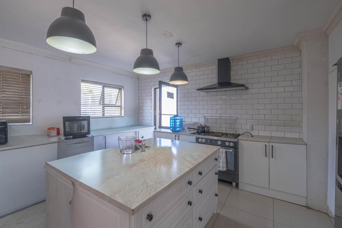 Modern kitchen featuring a central island with stone countertop, subway tile backsplash, gas stove with extractor, and ample built-in cabinetry.