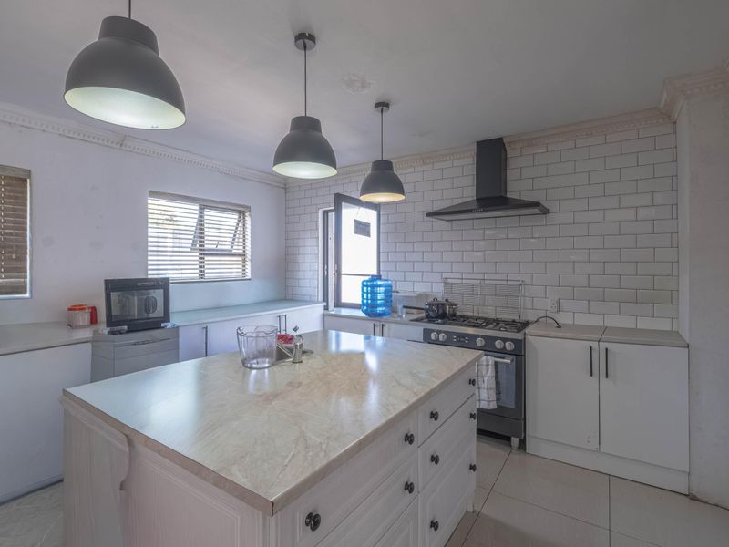 Modern kitchen featuring a central island with stone countertop, subway tile backsplash, gas stove with extractor, and ample built-in cabinetry.