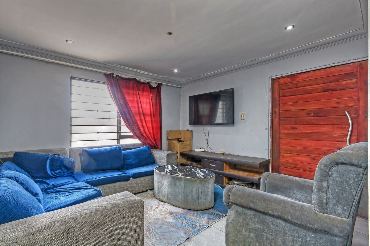 A living room featuring tiled flooring, recessed lighting, and a wooden door, currently requiring cosmetic updates to improve the overall finish and aesthetic appeal.