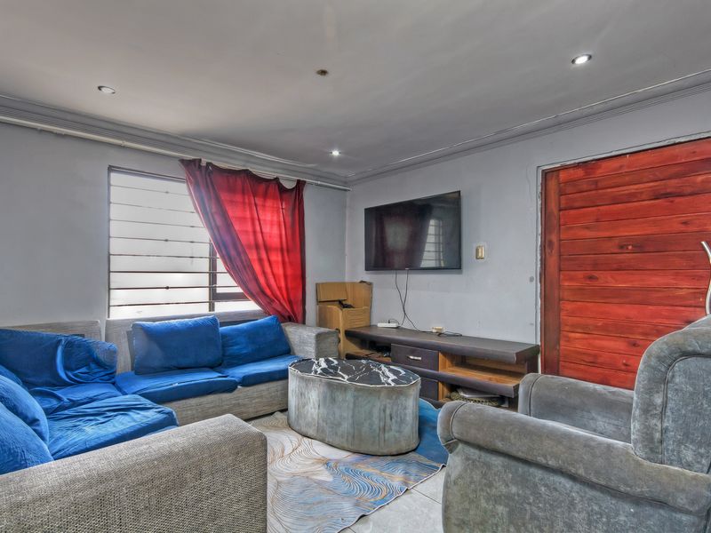 A living room featuring tiled flooring, recessed lighting, and a wooden door, currently requiring cosmetic updates to improve the overall finish and aesthetic appeal.