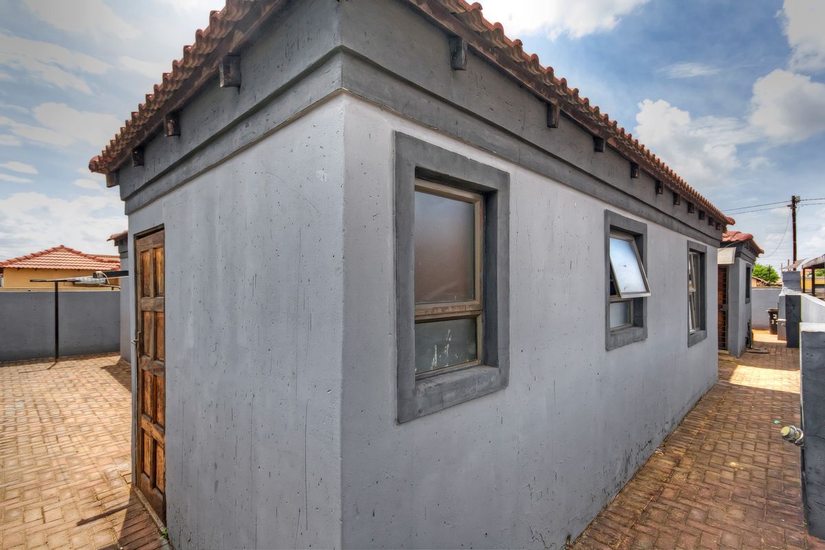 A view of the rear exterior of the property featuring plastered walls, terracotta roof tiles, and a paved courtyard area.