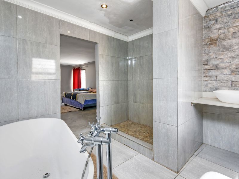 Modern bathroom featuring a freestanding bathtub, walk-in shower, and vessel sink with stone accent wall, showing some minor ceiling wear.