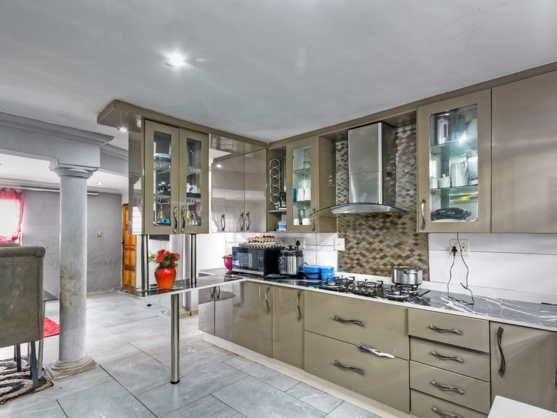 Modern kitchen featuring high-gloss cabinetry, stone countertops, gas hob, extractor fan, and a decorative tiled backsplash, integrated into an open-plan living space.