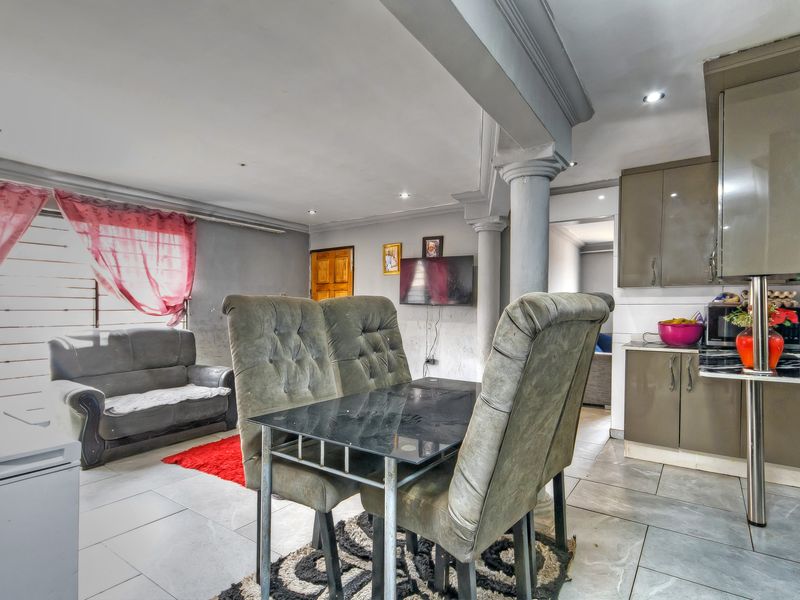 Open-plan living and kitchen area featuring tiled flooring, built-in cabinetry, and decorative columns, offering a functional layout with potential for cosmetic updates.