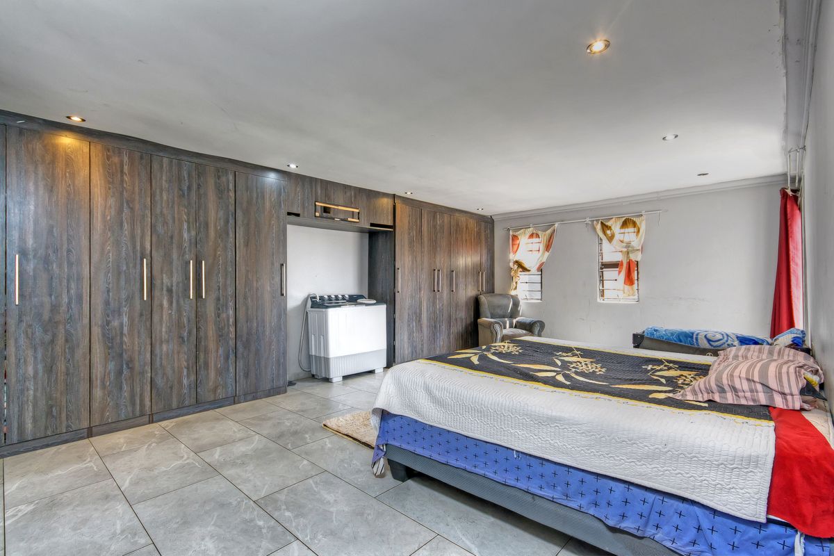 Spacious bedroom featuring extensive built-in wooden cupboards, tiled flooring, and recessed ceiling lighting, offering ample storage and a neutral foundation.