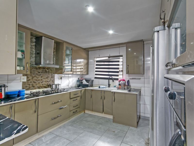 A functional kitchen featuring modern cabinetry, a gas hob with extractor, built-in wall ovens, and tiled finishes throughout.
