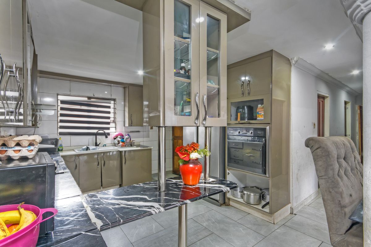 A functional kitchen featuring high-gloss cabinetry, marble-effect countertops, integrated oven, and tiled flooring, offering a practical layout for daily meal preparation.
