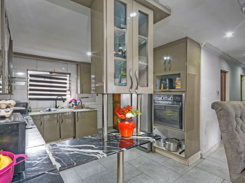 A functional kitchen featuring high-gloss cabinetry, marble-effect countertops, integrated oven, and tiled flooring, offering a practical layout for daily meal preparation.