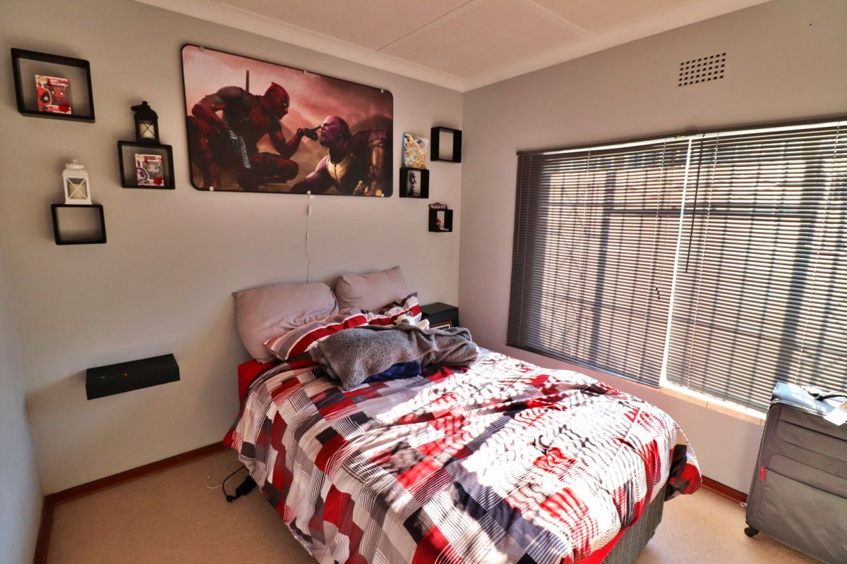 A functional bedroom featuring neutral wall finishes, carpeted flooring, and venetian blinds allowing natural light.