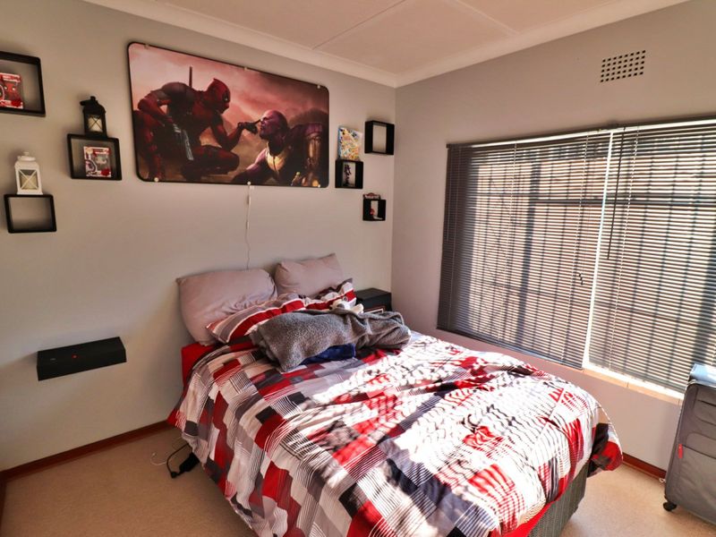 A functional bedroom featuring neutral wall finishes, carpeted flooring, and venetian blinds allowing natural light.