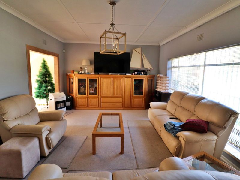 A comfortable living room featuring built-in wooden cabinetry, a central pendant light fixture, and large windows with venetian blinds.