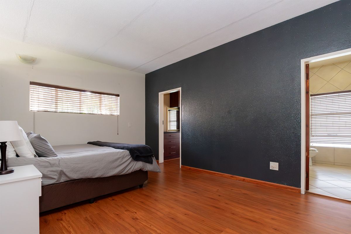 Spacious bedroom featuring laminate flooring, a dark textured accent wall, and direct access to an en-suite bathroom with tiled finishes.