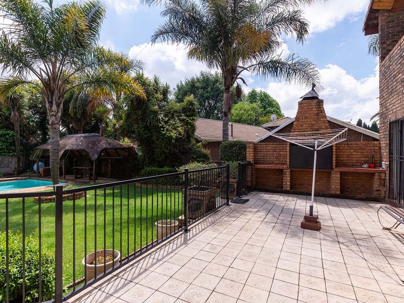 Spacious outdoor patio featuring a built-in brick braai, overlooking a well-maintained garden with a swimming pool and a charming thatched gazebo.