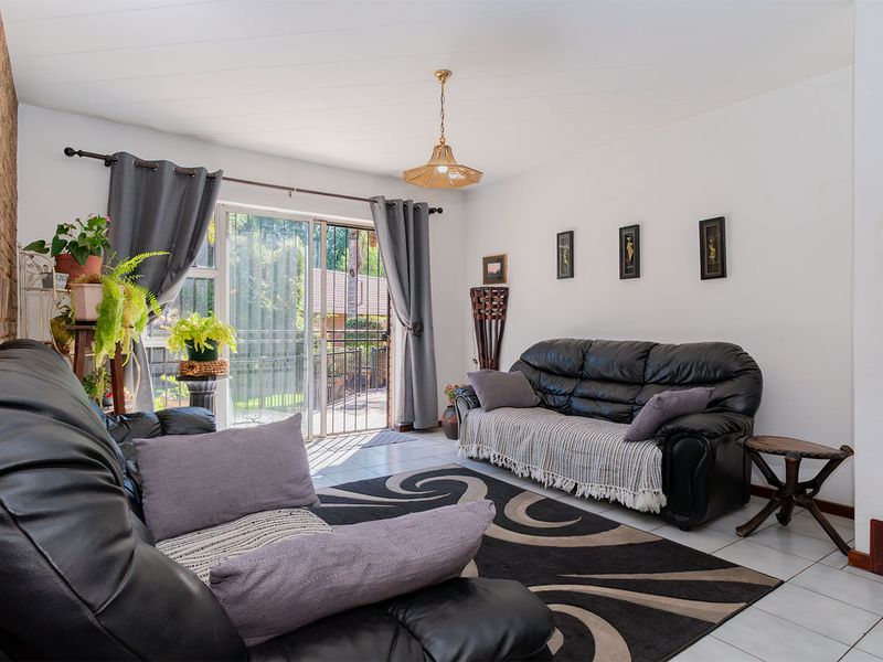 A bright living room featuring an exposed brick feature wall, tiled flooring, and a sliding glass door providing access to the outdoor area.