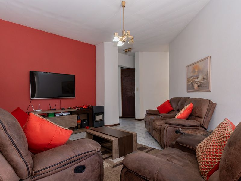 A living room featuring tiled flooring, a prominent red accent wall, and a central ceiling light fixture.