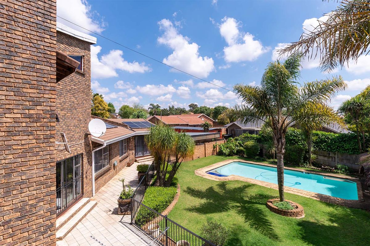 Rear view of the property featuring a brick facade, tiled patio area, swimming pool, and landscaped garden with established trees.