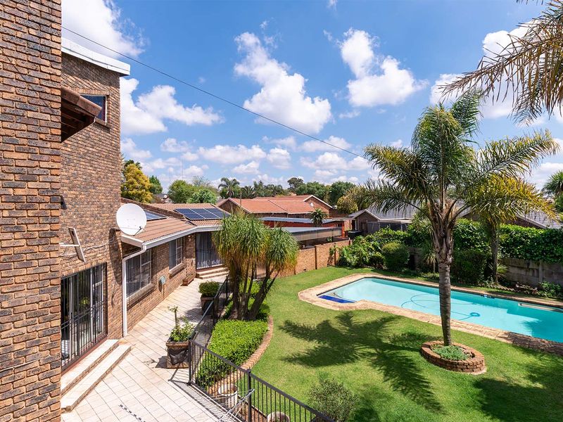 Rear view of the property featuring a brick facade, tiled patio area, swimming pool, and landscaped garden with established trees.