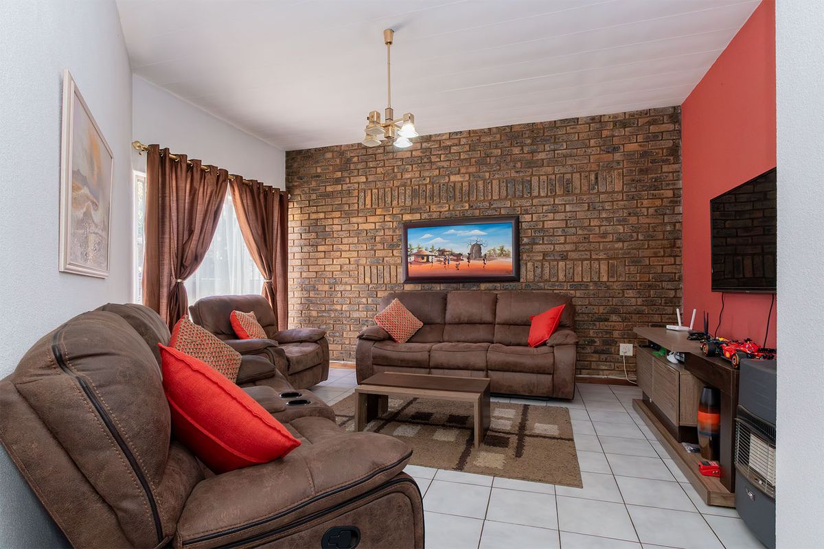 A comfortable living room featuring a prominent exposed brick feature wall, tiled flooring, and a classic tongue and groove ceiling.