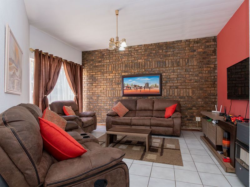 A comfortable living room featuring a prominent exposed brick feature wall, tiled flooring, and a classic tongue and groove ceiling.