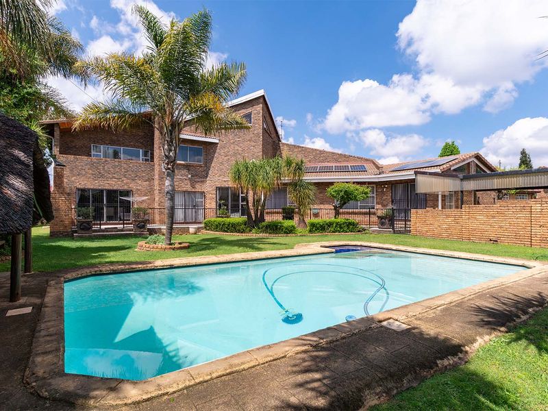 Spacious rear garden featuring a swimming pool, brick-faced multi-story residence, solar panels, and a traditional thatched lapa area.