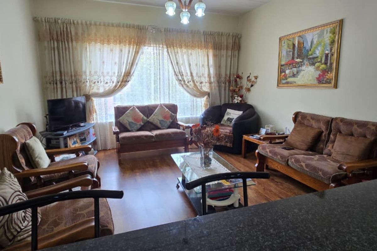 A comfortable living room featuring laminate flooring and natural light through large window curtains, providing a cozy and functional space.
