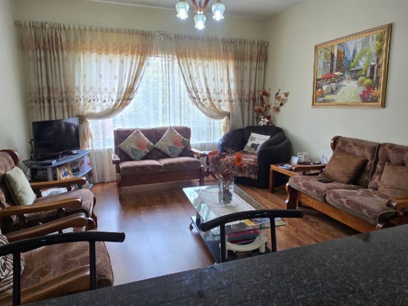 A comfortable living room featuring laminate flooring and natural light through large window curtains, providing a cozy and functional space.