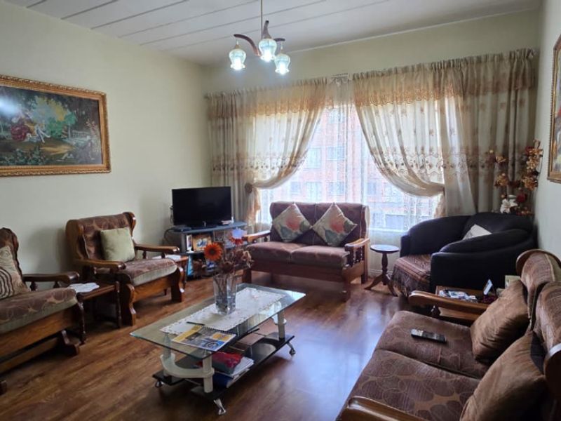A comfortable living room featuring laminate flooring and natural light through large window treatments.