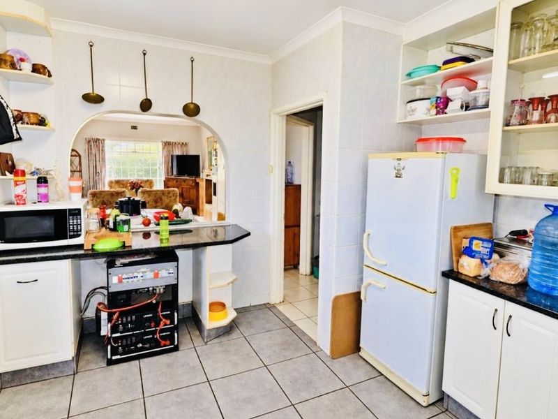 Functional kitchen featuring granite countertops, ample built-in cabinetry, and tiled flooring, with an open archway connecting to the adjacent living area.