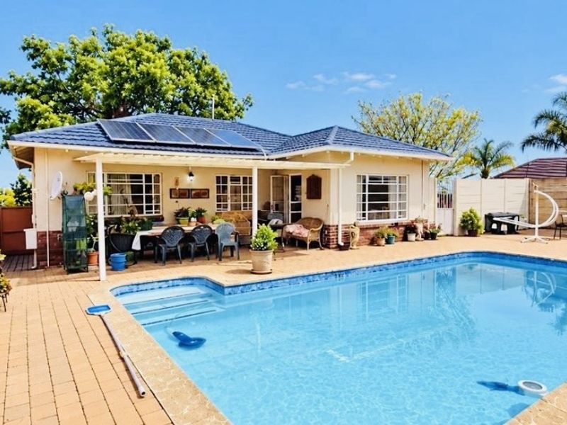 A well-maintained rear garden featuring a swimming pool, paved patio area, and solar panels installed on the tiled roof.
