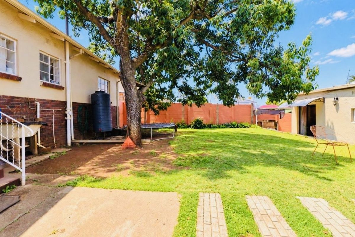 A spacious rear garden featuring a lawn, mature tree, brick boundary wall, and paved pathways, providing a functional outdoor area for the property.