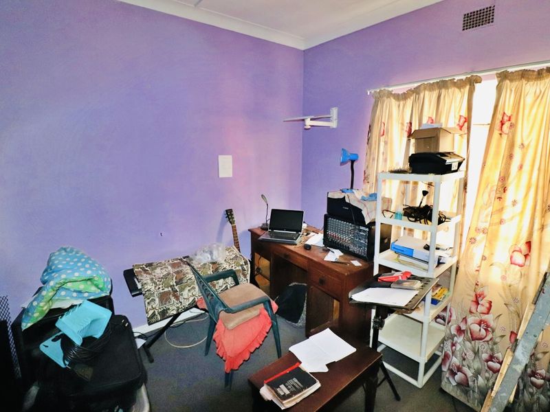 A bedroom space featuring purple walls, coving, and a wall-mounted air vent, currently utilized as a home office and storage area.
