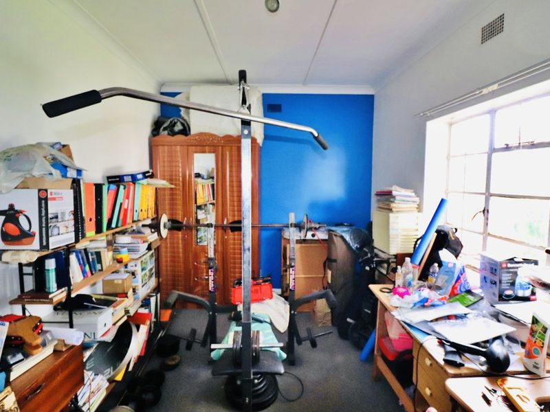 A multi-purpose bedroom space currently utilized as a home gym and storage area, featuring a large steel-framed window and blue accent wall.