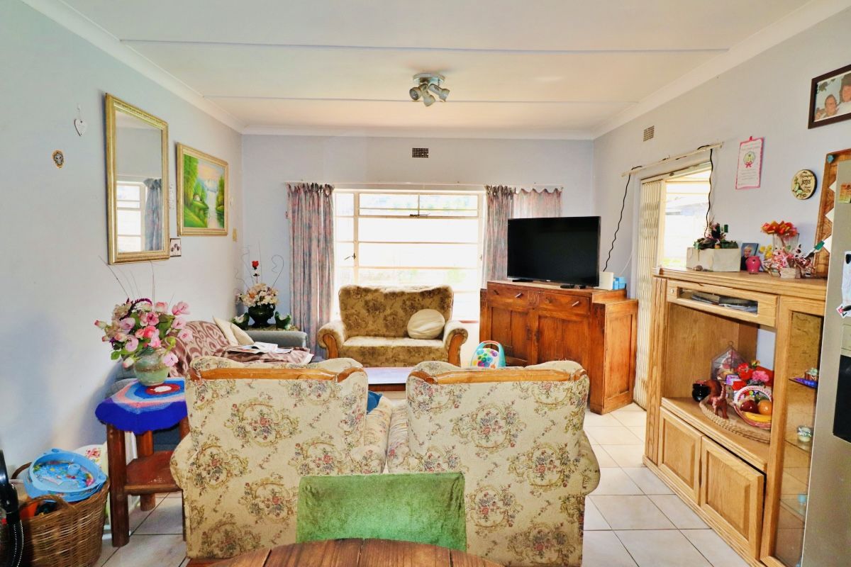 A spacious living room featuring tiled flooring, ceiling coving, and natural light provided by a large window and sliding glass door access.