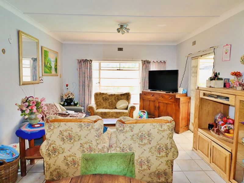 A spacious living room featuring tiled flooring, ceiling coving, and natural light provided by a large window and sliding glass door access.