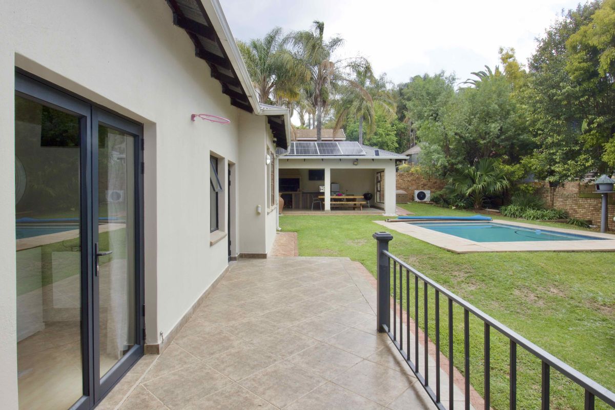 Rear view of the property featuring a tiled patio, swimming pool, landscaped garden, and a covered outdoor entertainment area with solar panels.
