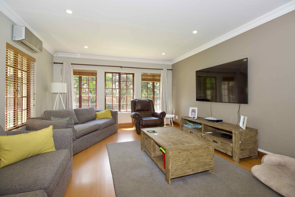 A well-maintained living room featuring timber flooring, recessed downlighting, and a split-system air conditioning unit.