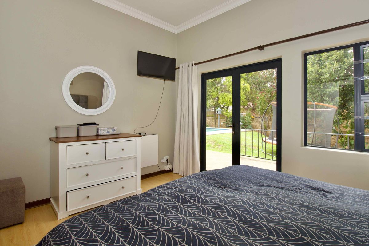 A well-lit bedroom featuring laminate flooring, a sliding glass door providing garden access, and large windows with aluminium frames.
