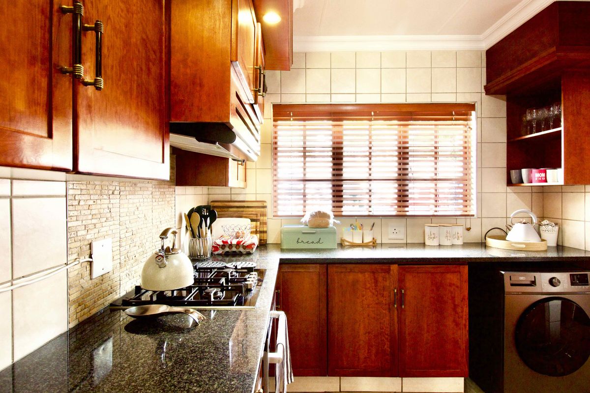 A functional kitchen featuring warm wooden cabinetry, granite countertops, a gas hob with extractor fan, and a tiled backsplash with integrated laundry space.